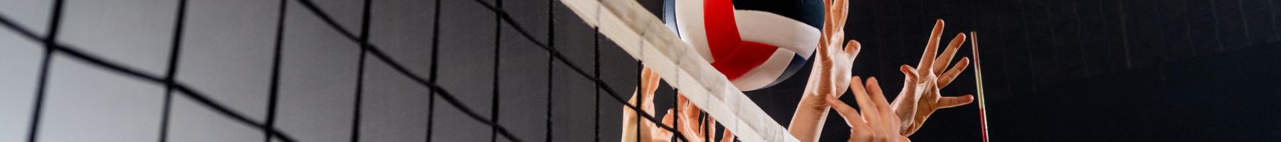 A photo of multiple hands reaching over a volleyball net to return the volleyball 